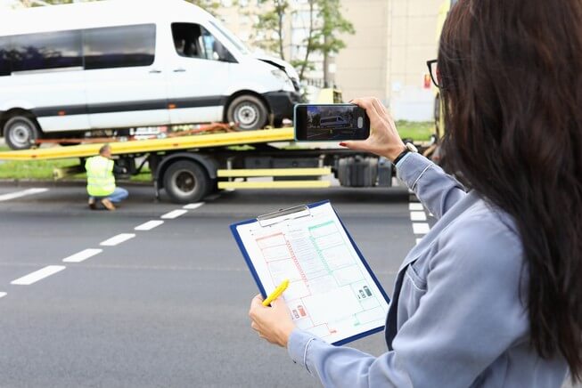 Woman takes picture of wrecked vehicle while holding a checkist 