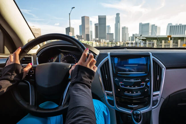 Woman drives car heading towards los angeles skyline 
